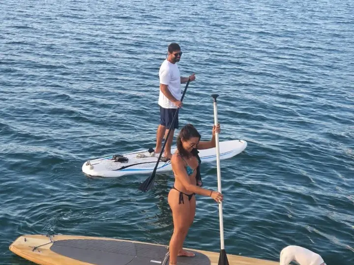 Casal remando em pranchas de stand up paddle ao lado da embarcação