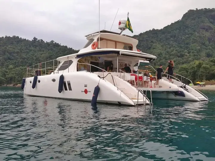 Catamarã ancorado em enseada de águas verdes, com convidados a bordo