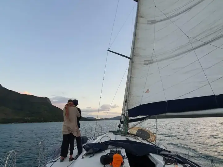 Casal na proa de um veleiro ao entardecer, com a vela aberta