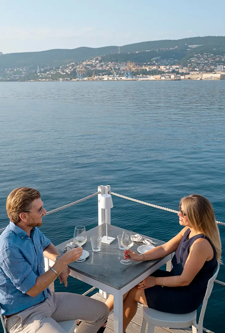Couple dining at a table on a yacht deck, with the sea behind them